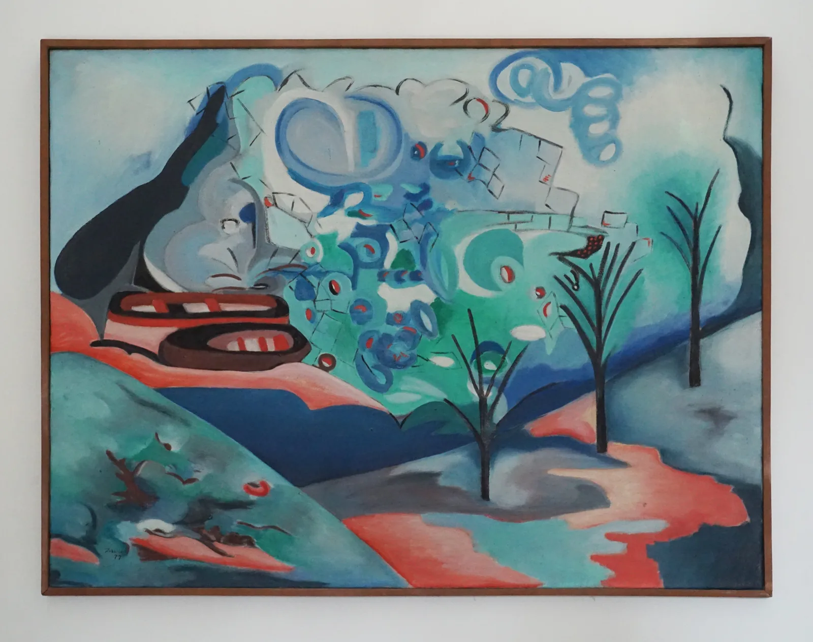 A framed horizontal abstract oil painting by pioneering modernist artist Zubeida Agha, rendered in a vivid surrealist style with cool blue, emerald green, coral, and deep navy tones. On the mid-left, two stylized, simplified brown and red boats rest against an undulating hill. The background dissolves into soft, cloud-like swirls of light blue and white, while a dense cluster of organic, circular patterns and mosaic-like shapes occupies the center. Bare, dark, skeletal tree structures anchor the right side of the canvas, rising from a landscape divided by a bright coral path or water stream, emphasizing the artist's signature interplay between structured geometry and deep philosophical emotion.