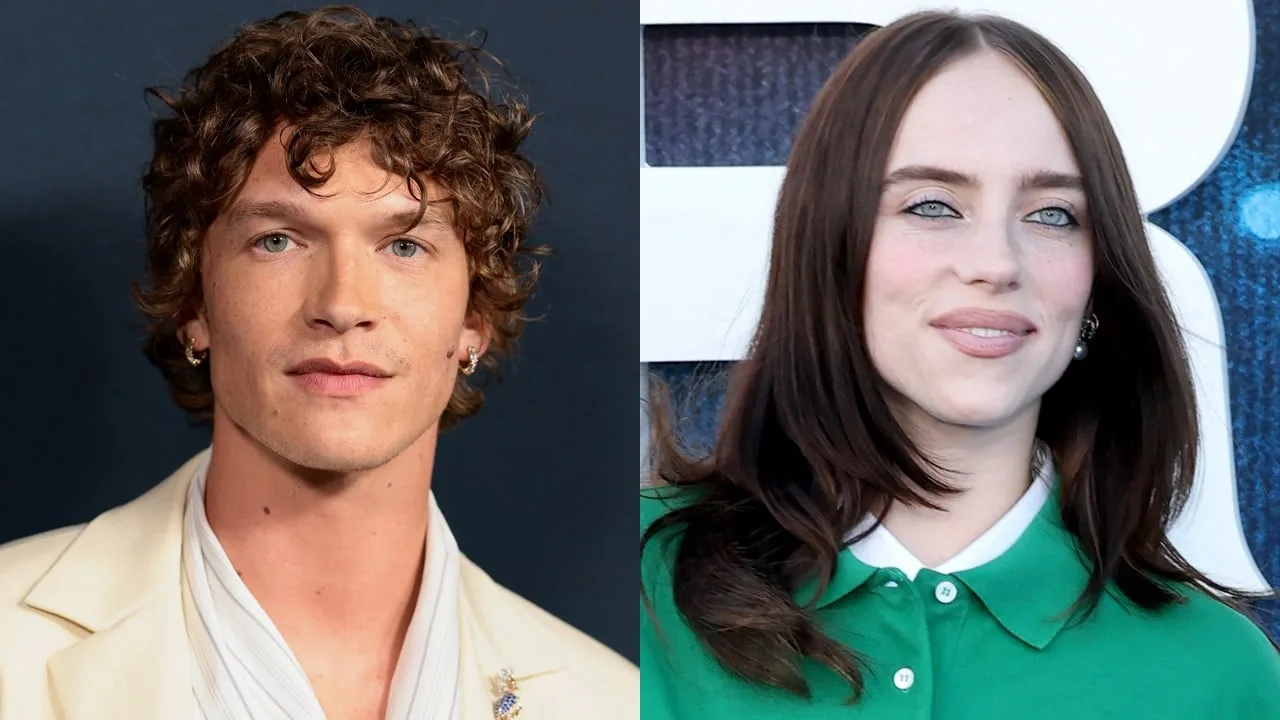 A side-by-side composite photo featuring actor Connor Storrie on the left and singer Billie Eilish on the right. On the left, Connor Storrie is shown from the chest up against a dark background, looking directly forward with a calm expression. He has short, curly brown hair, light blue eyes, and visible ear piercings, wearing a light cream-colored blazer over a draped white collared shirt. On the right, Billie Eilish is shown from the chest up, smiling gently at a slight angle against a blue-and-white background. She has straight, dark brown hair parted down the middle, distinctive light blue eyes with dark eyeliner, and is wearing a bright green polo shirt.