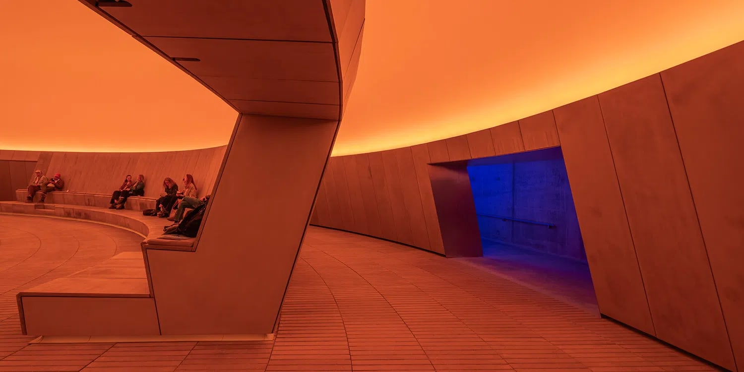 The permanent subterranean installation "As Seen Below—The Dome, a Skyspace" by James Turrell at the ARoS Aarhus Art Museum in Denmark is his largest museum Skyspace ever constructed. The 40-meter-wide structural dome features a massive 16-meter-wide ceiling aperture that acts as a direct, frame-free window to the sky.Inside, the minimal concrete arena leverages concealed LED sequences to shift colors, distorting viewers' depth perception and transforming the natural sky overhead into what appears to be a changing, solid plane of color.Key Architectural & Visual FeaturesSubterranean Structure: Built completely underground beneath the museum's lawn, acting as an introverted counterpart to the rooftop "Your rainbow panorama" by Olafur Eliasson.The Aperture: A central 16-meter circular opening that isolates a specific patch of the Danish sky.Dynamic Illumination: Hidden neon and LED lights flood the curved ceiling with hyper-saturated hues (such as deep oranges, stark blues, and pinks) to alter how the eye registers the natural light coming through the ceiling.Seating Perimeter: Smooth concrete benches line the outer circular wall, prompting visitors to recline and look directly upward.e's centre.
