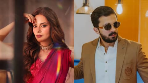 This split promotional banner showcases the lead cast members of an upcoming action-comedy film pairing Pakistani actress Amar Khan and content creator Rajab Butt together for the first time. On the left side, actress Amar Khan poses confidently, wearing an elegant, embellished rich magenta-red silk and chiffon saree paired with an intricate traditional gold choker necklace and matching stud earrings. Her look is completed with dramatic winged eyeliner, deep berry lipstick, and loose, glamorous waves framing her face. On the right side, YouTuber and influencer Rajab Butt leans against a pool table in a structured fawn-brown blazer accented with a distinct chest crest embroidery. He styles the jacket over a crisp white button-down shirt, a gold chain link necklace, and vintage round black sunglasses with a thick gold geometric frame. The background is warm and dimly lit, decorated with soft overhead pendant lights that bounce colorful prism-like lens flares across the entire visual layout.