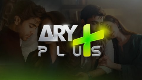The official logo of ARY Plus is prominently displayed in the center, featuring stylized silver lettering for "ARY" and "PLUS" with a large, glowing green plus sign intersecting the text, all set against a dimly lit background showing actors from promotional posters of Pakistani television dramas. A promotional graphic for the Pakistani entertainment television channel ARY Plus. The channel's logo sits centered in the foreground, showcasing the word "ARY" in bold, silver, block-style letters stacked above the word "PLUS" in a similar silver font. A large, vibrant lime-green plus symbol overlays the text, casting a soft yellow and green neon glow across the center of the image. The background is dark and translucent, revealing faint, emotional scenes from Pakistani drama posters. On the far left, a young man looks downward thoughtfully. In the center-right, a man and a woman are seated closely together, with the woman leaning her head gently against the man's shoulder in a somber, dramatic pose, representing scenes from the television serials "Dar-e-Nijaat" and "Bas Tera Saath Ho".
