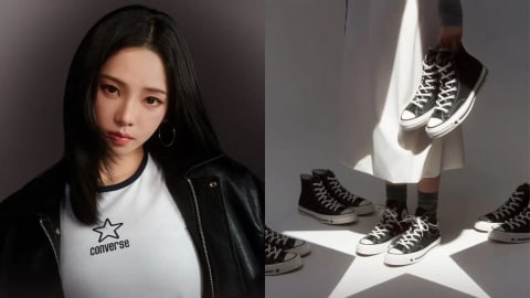 A split promotional image features K-pop star Karina from the group aespa as a global brand ambassador for the Converse Chuck 70 X sneaker collection. On the left side, Karina poses looking directly forward, styled with long black hair, hoop earrings, a black leather jacket, and a white ringer-style T-shirt displaying the star-shaped Converse logo. On the right side, an artistic product shot shows a model from the waist down wearing a long white skirt and mid-calf dark socks. A strong, crisp projection of a white Converse star shines on the floor beneath her feet. Several pairs of black high-top Chuck 70 X sneakers are arranged across the illuminated floor, while the model holds up an additional pair dangling next to the draped fabric of her skirt. The stark overhead lighting cast across the white skirt creates a sharp, triangular pattern of light and shadow.
