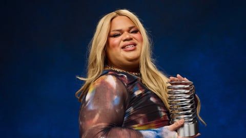Jools Lebron is an American TikTok creator and beauty influencer who achieved massive, overnight internet fame in August 2024 after coining the viral satirical phrase "very demure, very mindful". A transgender Latina woman of Puerto Rican heritage from Chicago, Lebron was working as a supermarket cashier and creating makeup tutorials before her video humorously detailing how to present oneself modestly in the workplace exploded into a global pop-culture phenomenon. The catchphrase took over social media, was adopted by countless major brands and celebrities, earned her a guest spot on Jimmy Kimmel Live!, and was ultimately named Dictionary.com's Word of the Year. Despite her rapid success—which initially allowed her to fund her gender transition and secure brand partnerships—the sudden lifestyle shift and overwhelming pressure of viral fame severely impacted her mental health, leading to public struggles with impulsive spending and substance abuse. Recently, Lebron faced significant internet backlash after launching a $45,000 GoFundMe campaign to repair dental rot caused by her past drug addiction. Though she quickly canceled the fundraiser and refunded her donors due to the criticism, the intense public scrutiny led her to announce a step back from TikTok to focus on her sobriety, recovery, and mental well-being away from the spotlight. A half-length studio portrait of social media creator Jools Lebron smiling warmly against a dark blue background. Lebron, a trans woman with long blonde hair, bright makeup, and bold eyeliner, is wearing a long-sleeved mesh top featuring a dark, colorful abstract print. She is standing in profile, turned toward the right side of the frame while looking back at the camera. In her hands, she proudly holds a silver, metallic trophy shaped like a large coil spring with a solid metal base. 