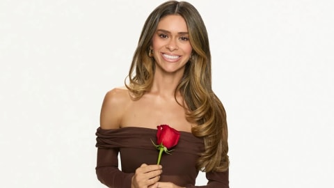 This promotional portrait captures Taylor Frankie Paul, one of the prominent reality television personalities starring in the Hulu docuseries The Secret Lives of Mormon Wives. Smiling brightly against a clean, minimalist white background, she is styled in an elegant, off-the-shoulder dark brown mesh long-sleeve dress that accentuates her long, voluminous honey-blonde waves. Holding a vibrant red rose vertically in front of her with both hands, the striking crimson flower acts as a stark, colorful contrast to the warm, earth-toned palette of her outfit, reminiscent of classic romance and reality dating show motifs.