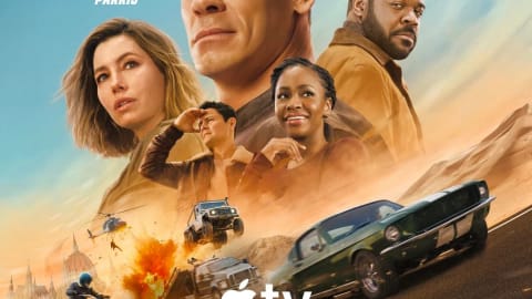 An official movie poster for the upcoming Apple Original Film, Matchbox, featuring a dramatic montage of the main cast set against a dusty, sun-drenched desert background. Dominating the upper center is a large portrait of John Cena looking resolute, flanked by Jessica Biel on the left and Sam Richardson on the right. Below them, smaller figures of Arturo Castro and Teyonah Parris are shown looking toward the horizon. The lower half of the poster is filled with high-octane action, showcasing a classic green muscle car racing forward, a rugged jeep navigating rough terrain, a motorcycle speeding away, and helicopters flying amidst explosive bursts. The prominent "Apple TV" logo sits just above the stylized, metallic title text "MATCHBOX THE MOVIE." The bottom text reveals it is an Apple Original Film by Skydance, rated PG-13, and announces "NEW MOVIE OCT 9."