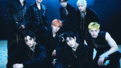 Stray Kids are pictured in a deep, underwater-inspired conceptual group portrait for their JAPAN 4th Mini Album『SUIATSU』, capturing a mysterious, siren-like aesthetic ahead of its official release on November 25, 2026. Dressed in highly structured dark outfits embellished with metallic hardware, shimmering chains, and draped pearl networks, the eight members—Bang Chan, Lee Know, Changbin, Hyunjin, Han, Felix, Seungmin, and I.N—pose submerged against a dark blue marine backdrop filled with floating bubbles. Above the group, the album's title SUIATSU (meaning water pressure) is rendered in a distorted, liquid chrome typeface that flows across the top of the jacket image.