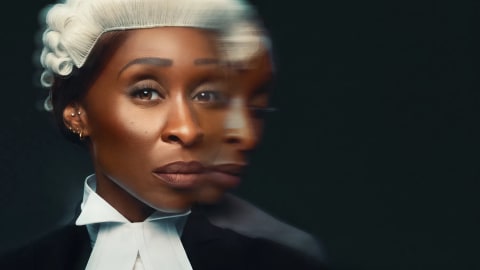 This close-up promotional image features British actress Cynthia Erivo portraying the protagonist Tessa Ensler in the 2026 film adaptation of Prima Facie. She is dressed in traditional British courtroom attire, wearing a stark white collared shirt, prominent white bands (tabs), and a dark judicial robe. Atop her head sits a traditional white curled legal wig. Her expression is stern, intensely focused, and solemn, reflecting the dramatic weight of the story. A distinctive motion-blur overlay effect is applied to her profile, creating a ghosted, layered double-image silhouette that trails off to the right. This visual effect powerfully symbolizes her internal conflict, fractured sense of reality, and the duality of transitioning from a confident defense attorney to a vulnerable witness navigating a flawed legal system. The deep, dark backdrop provides a sharp contrast that makes the legal garb and her piercing gaze the central focus of the frame.