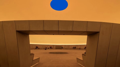 American artist James Turrell has created As Seen Below, a 40-metre-wide Skyspace, for the ARoS Aarhus Art Museum in Aarhus, Denmark.  Opening today, the domed extension realised in collaboration with Danish studio Schmidt Hammer Lassen, is an immersive subterranean space washed in monochromatic colours.  A six-metre-wide central aperture sits at the dome's apex to frame views of the shifting sky above.  As Seen Below by James Turrell James Turrell has created a 40-metre-wide Skyspace for the ARoS Aarhus Art Museum "In As Seen Below, I'm shaping the experience of seeing rather than delivering an image," the artist explained.  "The architecture holds the sky close, so you recognize that the act of looking is the work itself."  "Here, light isn't description, it's the substance you stand within," he added.  As Seen Below by James Turrell It sits beside the museum's original building The installation's opening marks the completion of the museum's wider 4,000-square-metre expansion led by Schmidt Hammer Lassen, for which Turrell's Skyspace is the "centrepiece".  As Seen Below is the artist's 100th Skyspace installation and, according to the museum, his most ambitious one yet.  As Seen Below by James Turrell A six-metre-wide aperture frames views of the sky The installation connects to the main museum building both above and below ground via a new outdoor exhibition space and subterranean corridor respectively.  Above ground, the structure emerges from the museum's park as a grass-covered mound.  Its volume is topped with a 100-square-metre operable lid that allows the oculus to be closed and double as a lighting system.  As Seen Below by James Turrell Its interior is washed in monochromatic colours Ground level access to the space is provided by an arched concrete opening that carves into the structure.  Inside, the 16-metre-tall dome is centred around a sweeping open space, which is entered through gaps in a secondary concrete structure that provides stepped seating.  The interior has been finished with a grey-toned material palette of raw concrete and brick paving, which slopes down to a stone-covered drainage area at the structure's centre.
