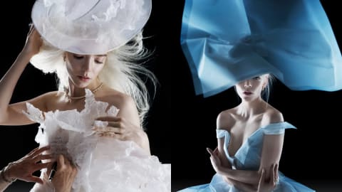 An image collage shows actress Anya Taylor-Joy posing in avant-garde, ethereal garments made from textured paper against a stark black background. On the left, she looks downward while wearing an elaborate, translucent white paper hat and a ruffled white paper gown. Another person's hands are visible in the lower left corner, writing text onto the bodice of her dress with a marker. Her blonde hair is styled in a voluminous, wind-blown fashion, and she wears a delicate gold chain necklace. On the right, she faces forward, wearing an architectural, oversized blue paper headpiece that partially veils her face, paired with an off-the-shoulder light blue paper dress. Her hair is tied back, and the dramatic side-lighting highlights the sculptural qualities and crisp folds of both outfits.