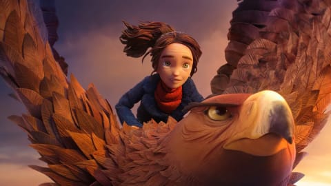 A high-angle, cinematic promotional still captured from LAIKA Studios' stop-motion animated feature film Wildwood, centers on the headstrong teenage protagonist Prue McKeel (voiced by Peyton Elizabeth Lee) soaring gracefully through the clouds while riding atop the General (voiced by Angela Bassett), a formidable and massive golden eagle. The young girl, with wide green eyes, an intense yet hopeful expression, and her dark brown hair tied back in a windswept ponytail, leans slightly forward over the creature's broad back while wearing a textured, dark navy blue coat layered over a thick red knit scarf. The giant avian character dominates the lower half of the frame, showcasing an exceptionally detailed face with an amber-ringed, fierce eye, a curved dark-tipped yellow beak, and a magnificent layer of thousands of individually handcrafted, overlapping polysatin feathers meticulously arranged in warm shades of copper, gold, and light brown. A soft, dramatic golden-hour sunlight bathes the upper surface of the eagle's outstretched wings and illuminates the misty cloudscape in the background, creating a vibrant contrast against the cooler, overcast purple and grey twilight tones blanketing the sky behind them.