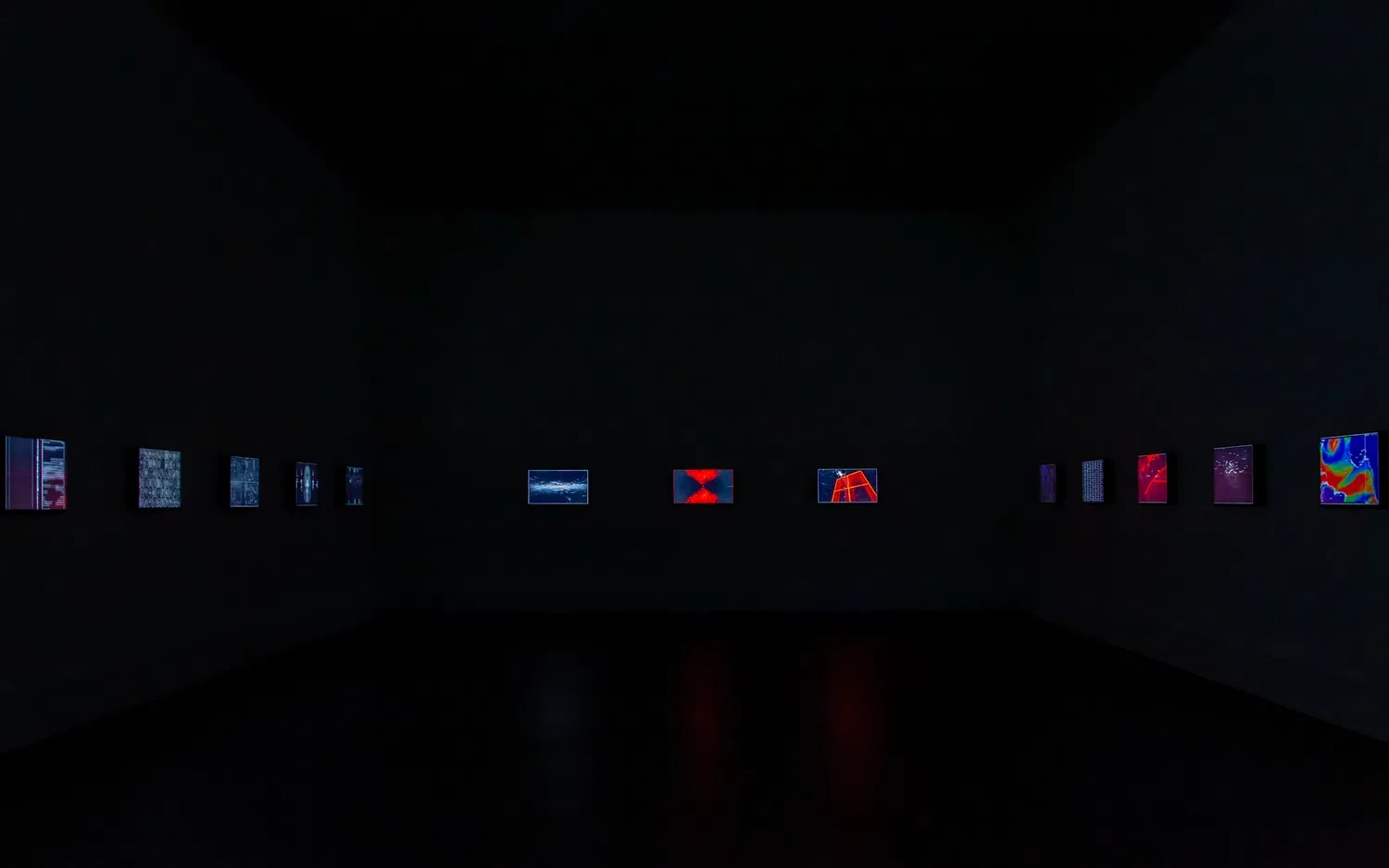 Dark gallery room in Zero 10's Event Hall displaying small colorful digital artworks along the walls