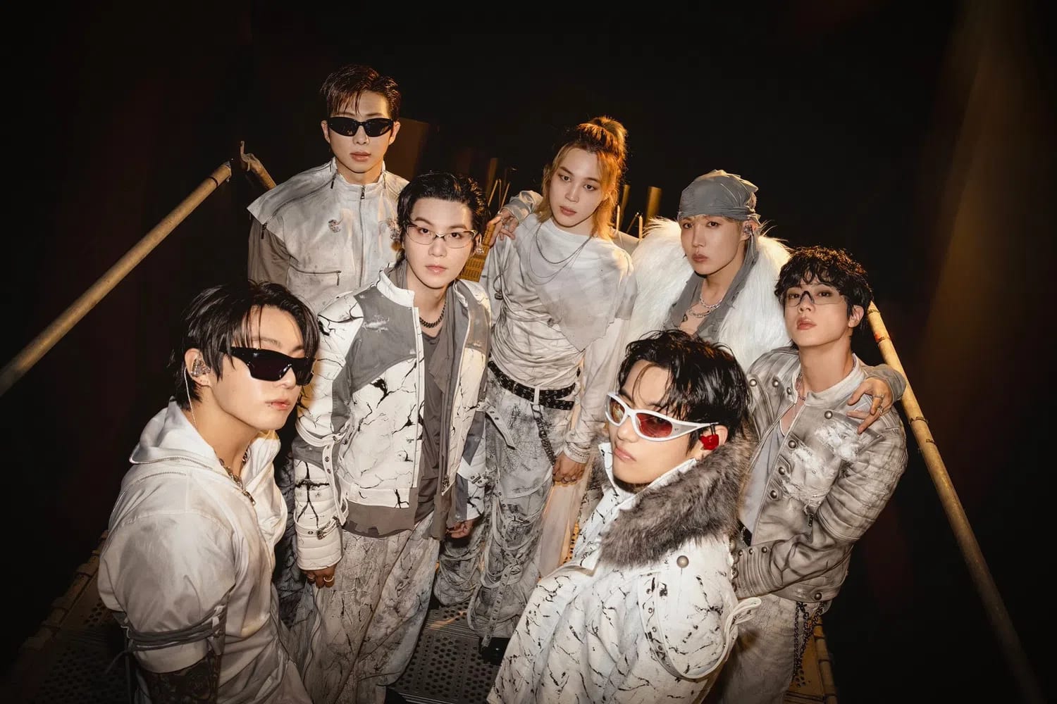 The global icons are pictured posing together behind the scenes at Estadio San Marcos. The K-pop supergroup BTS [Entity] is captured backstage during the South American leg of their highly anticipated global comeback series. Members RM, Jin, SUGA, j-hope, Jimin, V, and Jung Kook stand tightly grouped under dramatic backstage lighting, modeling an avant-garde ensemble of coordinated monochrome outfits. Their stage attire features intricate black-and-white splattered and distressed patterns, layered over textured white and cream fabrics, complemented by distinct dark sunglasses worn by several members.