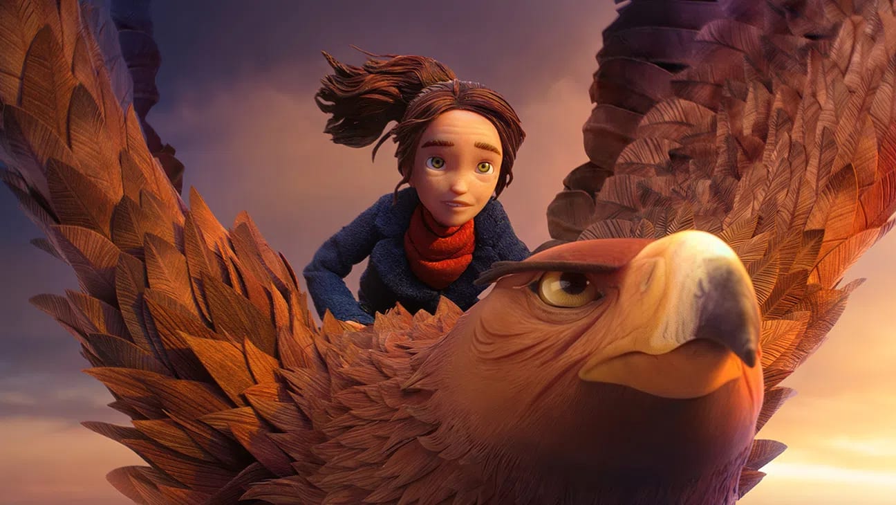 A high-angle, cinematic promotional still captured from LAIKA Studios' stop-motion animated feature film Wildwood, centers on the headstrong teenage protagonist Prue McKeel (voiced by Peyton Elizabeth Lee) soaring gracefully through the clouds while riding atop the General (voiced by Angela Bassett), a formidable and massive golden eagle. The young girl, with wide green eyes, an intense yet hopeful expression, and her dark brown hair tied back in a windswept ponytail, leans slightly forward over the creature's broad back while wearing a textured, dark navy blue coat layered over a thick red knit scarf. The giant avian character dominates the lower half of the frame, showcasing an exceptionally detailed face with an amber-ringed, fierce eye, a curved dark-tipped yellow beak, and a magnificent layer of thousands of individually handcrafted, overlapping polysatin feathers meticulously arranged in warm shades of copper, gold, and light brown. A soft, dramatic golden-hour sunlight bathes the upper surface of the eagle's outstretched wings and illuminates the misty cloudscape in the background, creating a vibrant contrast against the cooler, overcast purple and grey twilight tones blanketing the sky behind them.