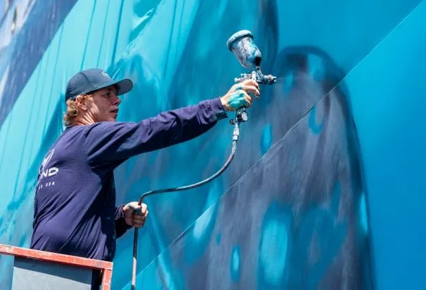 Laguna Beach artist, Wyland, one of the best-known marine-life painters in the country, uses a paint sprayer to recreate the first of his 100 whaling walls on a giant canvas adjacent to his gallery in Laguna Beach on Monday, July 15, 2019, 38 years after he first painted the mural on the Hotel Laguna. (Photo by Leonard Ortiz, Orange County Register/SCNG)