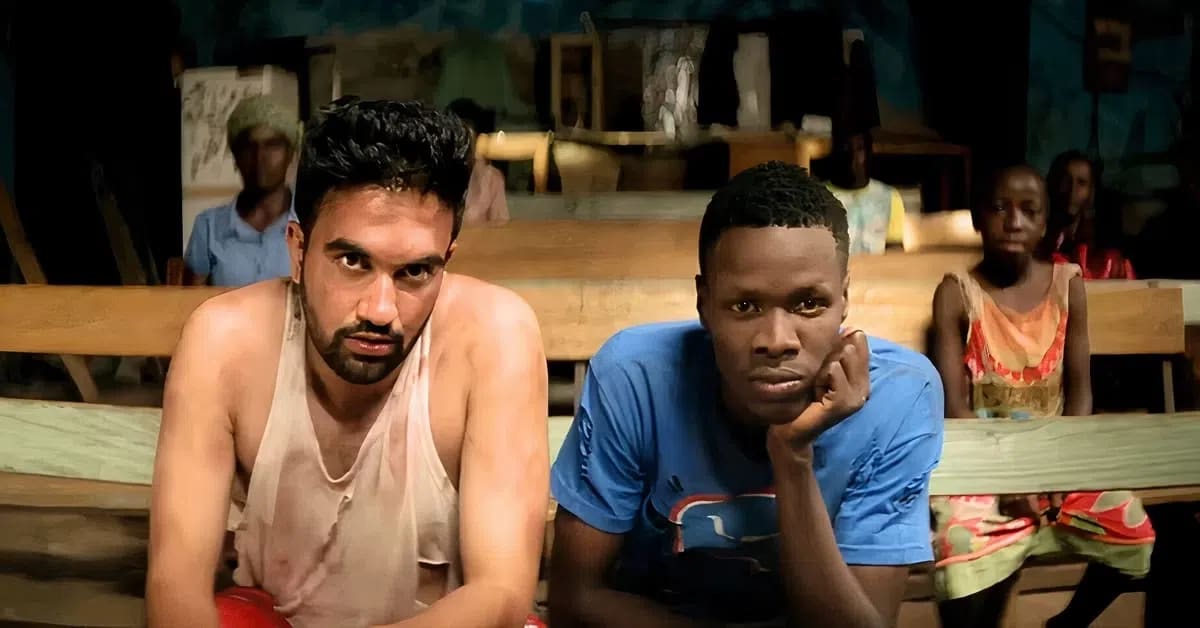 This image features future New York City Mayor Zohran Mamdani during his appearance in Disney's biographical sports drama film, Queen of Katwe (2016). Long before stepping into City Hall as NYC’s 111th mayor, Mamdani worked extensively behind the scenes on the movie directed by his mother, Mira Nair. He took on multiple roles for the production, including serving as an assistant director and music supervisor, performing a rap track under the pseudonym "Young Cardamom", and making a cameo appearance onscreen. In this specific scene, he portrays a character credited as a "Bookie Student" sitting alongside another young man on wooden benches in a rustic room.