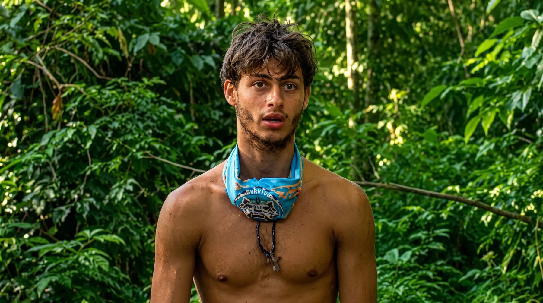 A medium close-up shot captures Stavros Floros, a contestant from the 13th season of the reality TV show Survivor Greece, standing shirt-less in front of a dense, lush green jungle backdrop. He is looking slightly off-camera to his right with an open-mouthed, intense expression. He wears a light blue Survivor buff rolled around his neck like a collar, with a dark cord necklace holding a small cross pendant dangling down his chest. The bright, natural sunlight filters through the green foliage, illuminating his disheveled brown hair, stubble, and sun-tanned shoulders while casting soft shadows across his torso.