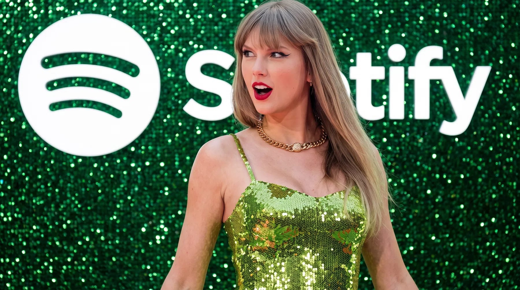 Taylor Swift sports a vibrant, lime-green sequined dress paired with a chunky gold chain necklace as she poses dynamically in front of a sparkling green backdrop adorned with the Spotify logo. Her long blonde hair is styled straight with signature full bangs, and her striking makeup features a sharp, black winged eyeliner and a bold, classic red lip. Her expression is playful and animated, captured mid-glance to the side with an open-mouthed, surprised look that adds a lively, candid energy to the red carpet event. The dress's thin spaghetti straps and scoop neckline showcase the prominent necklace, while the textured, shimmering wall behind her reflects countless pinpricks of light, matching the glitter of her outfit and amplifying the festive, high-profile atmosphere of the occasion.