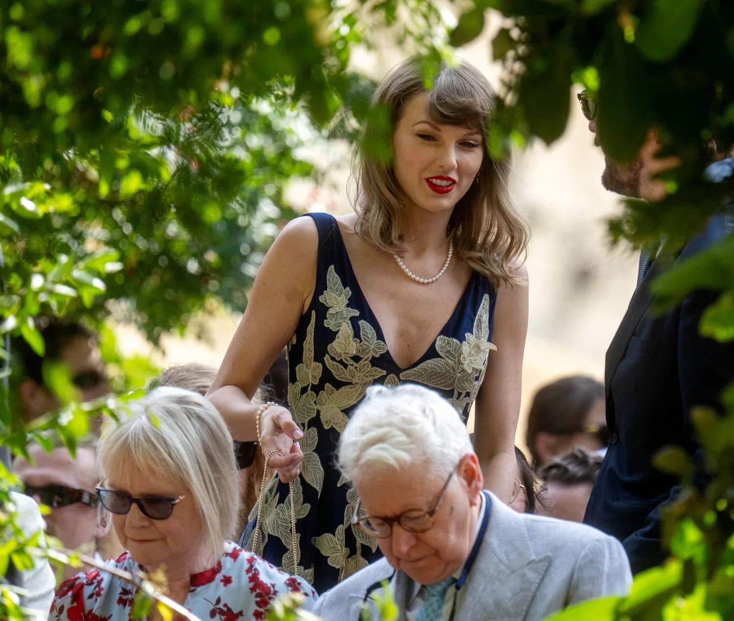 Taylor Swift turned heads while attending the star-studded wedding of her longtime recording engineers, Laura Sisk and Oli Jacobs, on Saturday, August 15, 2026, at Peter Gabriel's legendary Real World Studios in Bath, Gloucestershire, England. Attending the intimate ceremony solo while her husband, Travis Kelce, prepared for a Kansas City Chiefs preseason game, Swift officially debuted her shortest haircut in years—a chic, wavy, shoulder-length bob paired with her iconic straight bangs. She complemented the dramatic new look with a plunging navy blue Costarellos dress featuring intricate gold floral embroidery, a pearl necklace, and her signature bold red lip. Fans and media closely observed her jewelry as she proudly showcased her massive engagement ring and new gold wedding band following her own highly anticipated wedding to Kelce at Madison Square Garden just weeks prior in July. Because Sisk and Jacobs are highly accomplished, Grammy-winning studio professionals who have engineered tracks across multiple eras of Swift's discography, the celebration doubled as a powerhouse music reunion where Swift spent the evening socializing with close friends and prominent musical collaborators, including Jack Antonoff, Sabrina Carpenter, and Phoebe Bridgers.
