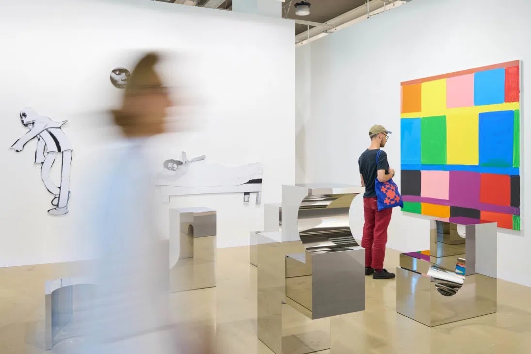 Visitors browse stainless steel sculptures and colorful grid paintings on the Art Basel 2026 fair floor at Messe Basel  Credit: Photo: Art Basel  Place: In "The Cautious Register of Money" section, after "Inside the main galleries, the word most often heard during the first day of the VIP preview was not 'sold'..."